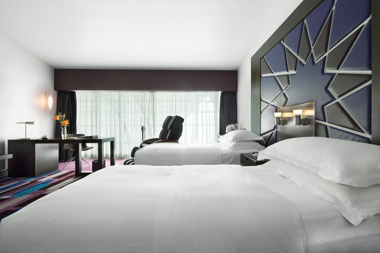 Dubai International Terminal Hotel Exterior photo The photo shows a modern hotel room featuring two beds with white linens. There's a large window with sheer curtains that allows natural light to fill the space. One bed is positioned next to a stylish wall design with a geometric pattern. A small de