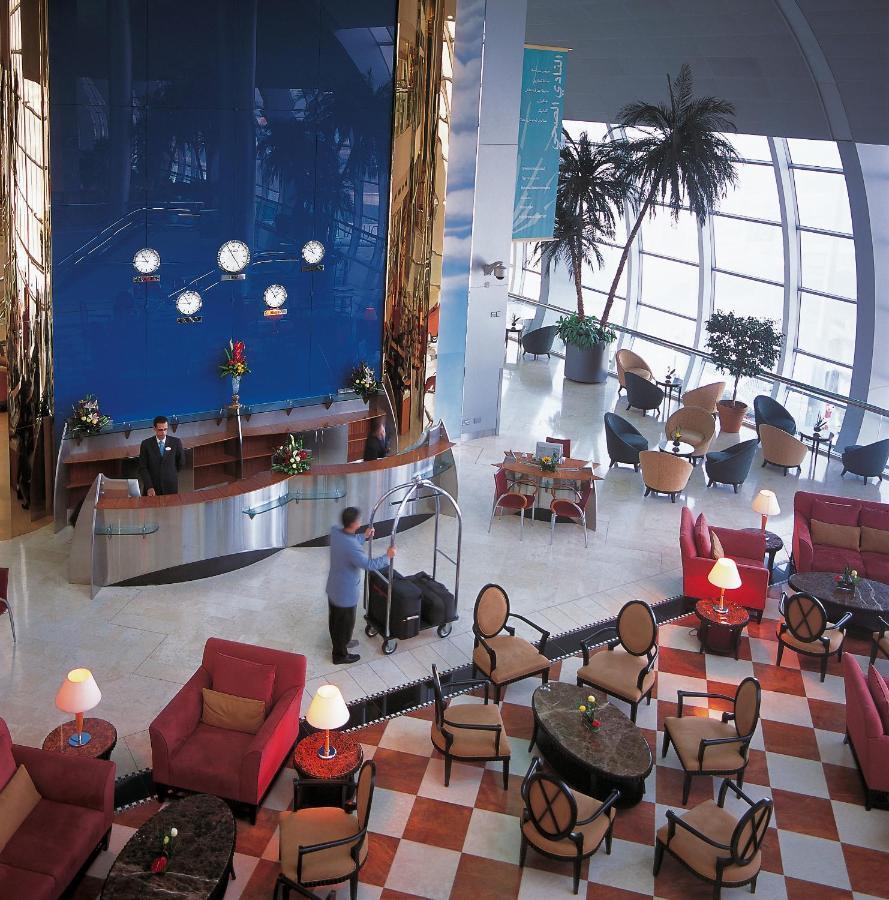 Dubai International Terminal Hotel Exterior photo The photo depicts a hotel lobby that features elegant decor and modern design elements. In the foreground, there are several red armchairs and tables arranged in a comfortable seating area. The floor has a checkerboard pattern, contributing to the up